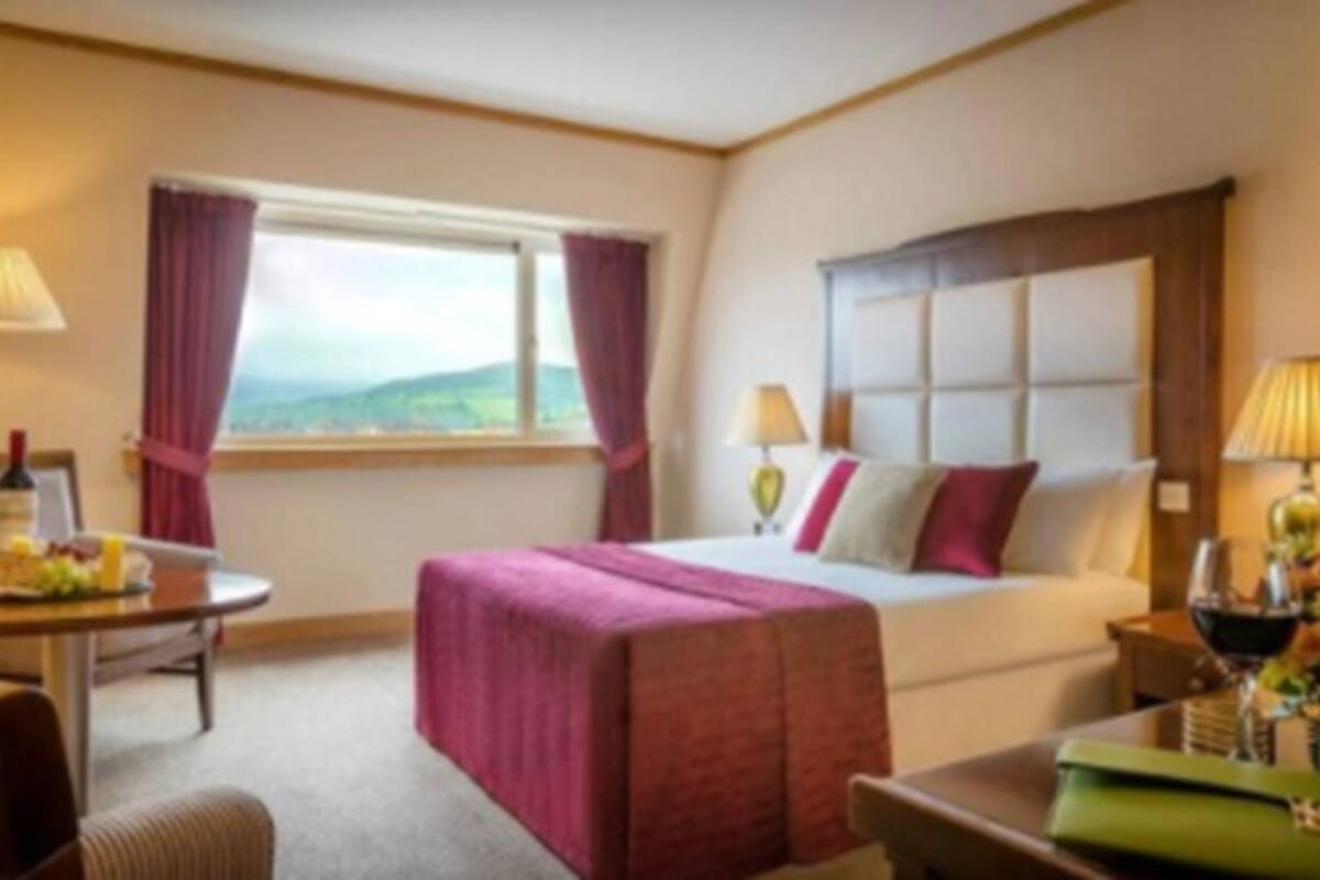 A hotel room with a bed, a desk, a chair, a window with curtains, and a view of the outdoors.