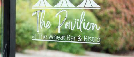 Une fenêtre sur laquelle est apposée une enseigne indiquant : « Le Pavillon du Wheat Bar & Bistro ».