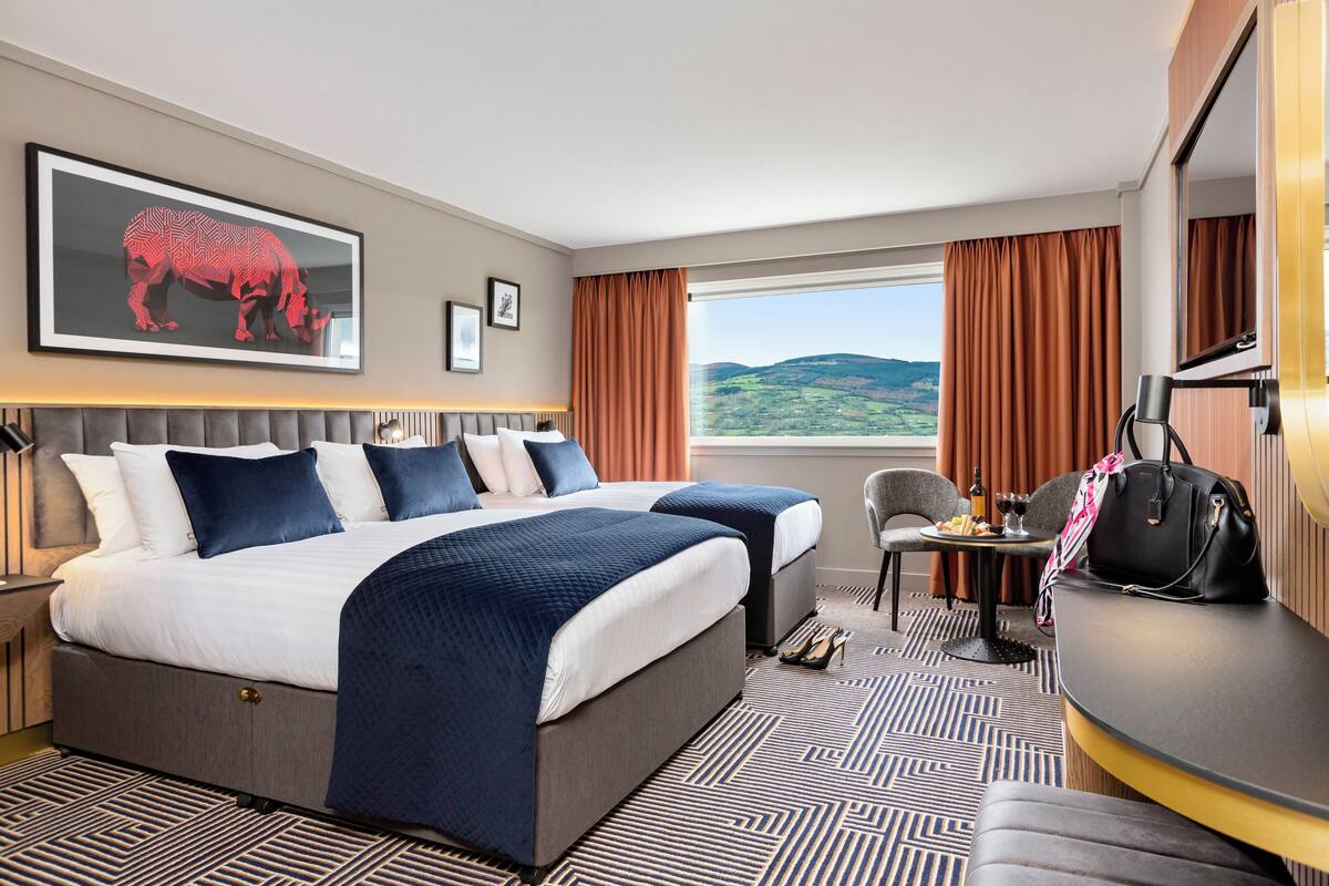 A hotel room with a large bed, a desk, a chair, and a view of the outdoors.