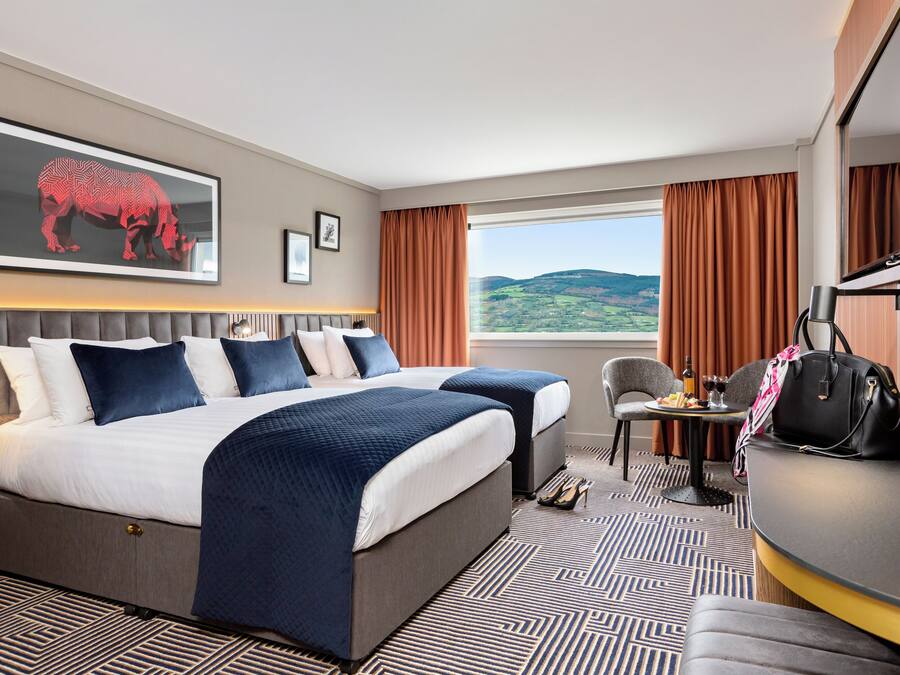 A hotel room with a large bed, a desk, a chair, and a view of the outdoors.