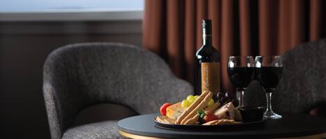 Une table avec une bouteille de vin, deux verres et une assiette de fromage, de crackers et de raisins.