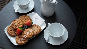 Ein runder Tisch mit einem weißen Teller Kekse und Erdbeeren, einer weißen Teekanne und zwei weißen Tassen mit Untertassen.