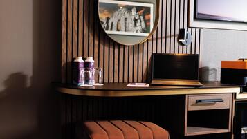 A hotel room with a wooden panel wall, a round mirror, a laptop, a coffee maker, and a cushioned chair.