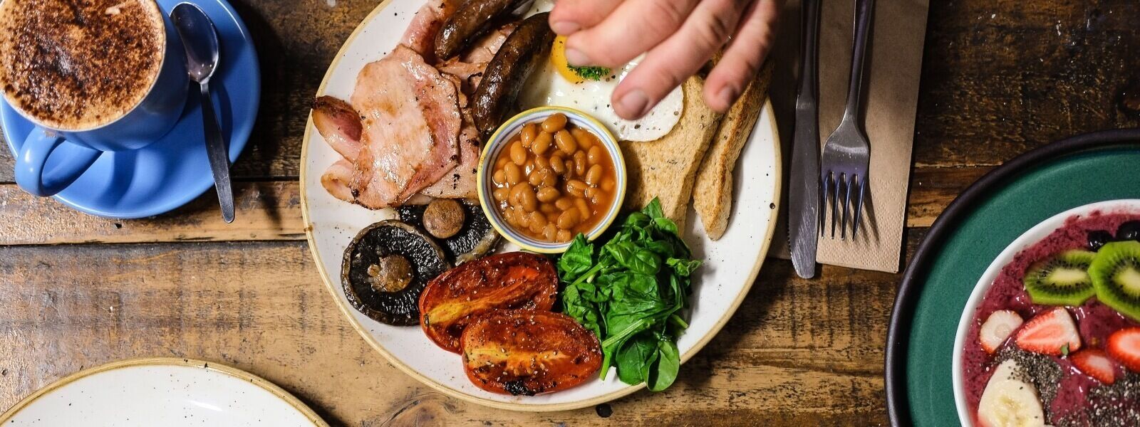 Un plat amb diferents aliments, com ara fesols, verdura de fulla i talls de carn, acompanyat d'una tassa de cafè.