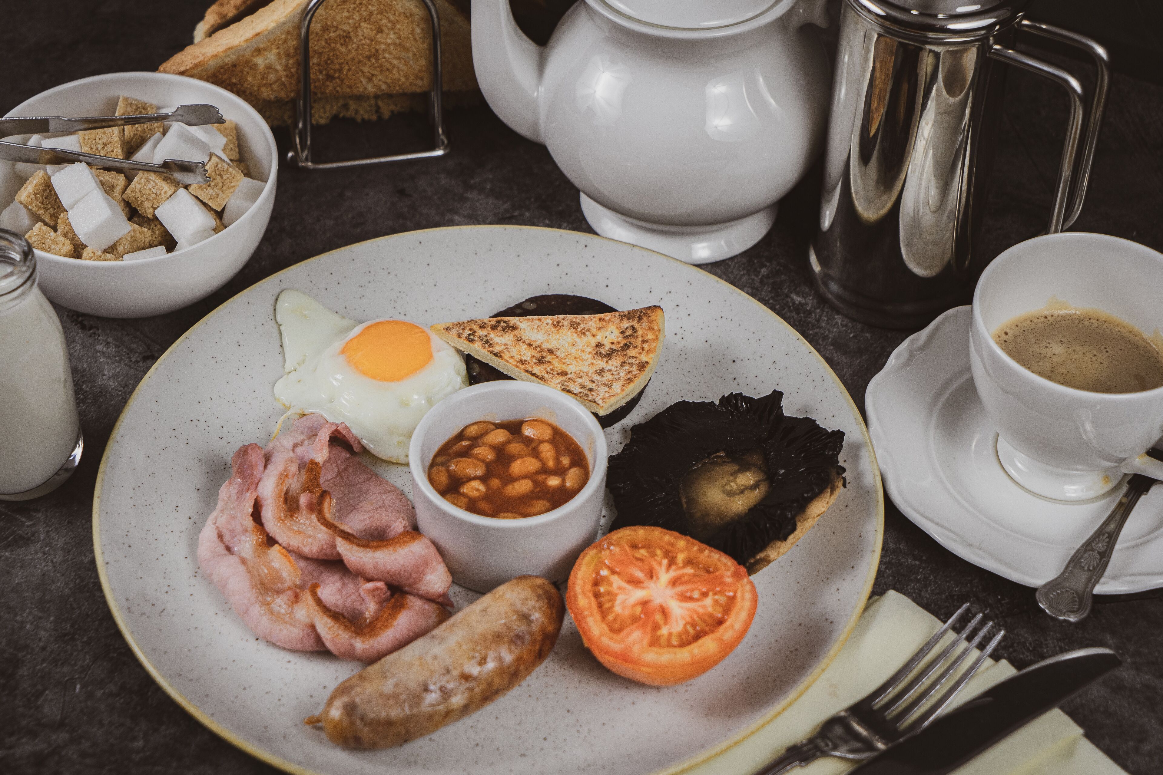 Un plato de desayuno con huevos, tocino, salchichas, tostadas, frijoles y tomate.