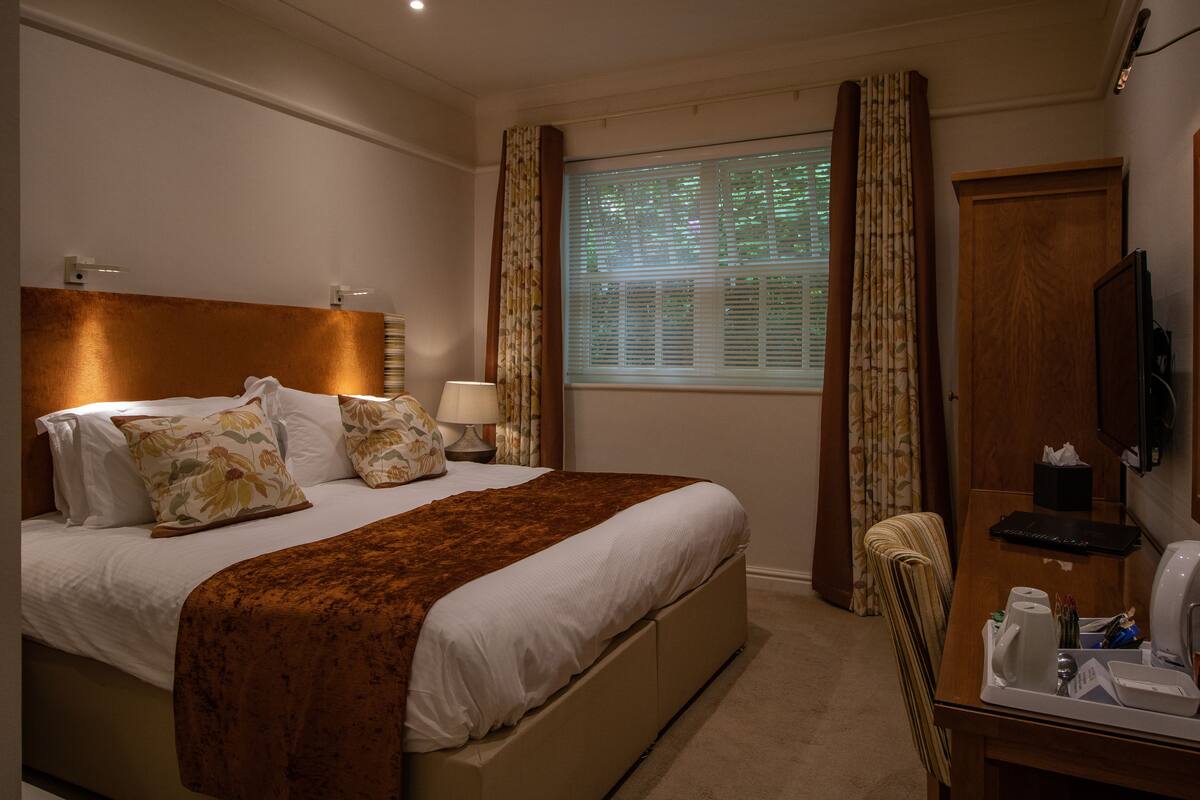 Een hotelkamer met een bed, nachtkastje, lamp en televisie.