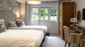 Een hotelkamer met twee bedden, een bureau, een stoel, een groot raam en een houten garderobe.