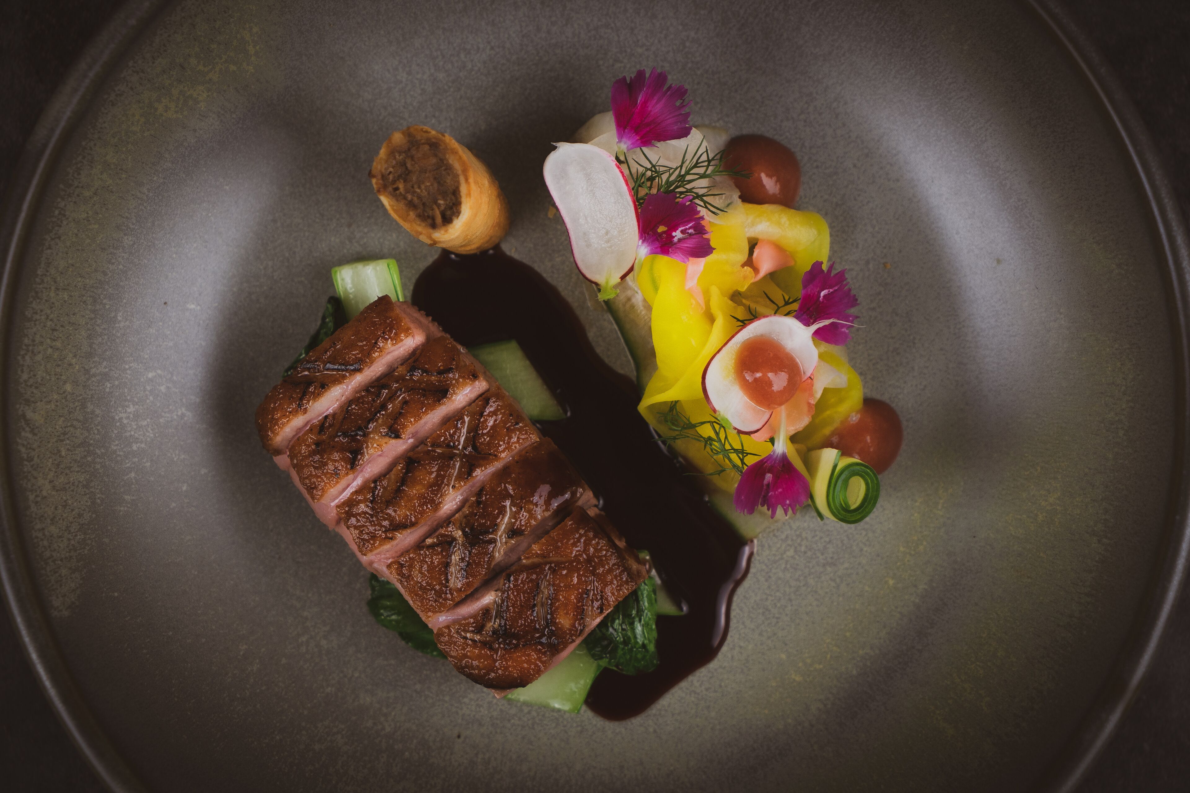 Un plato con carne a la parrilla, verduras y una decoración floral.