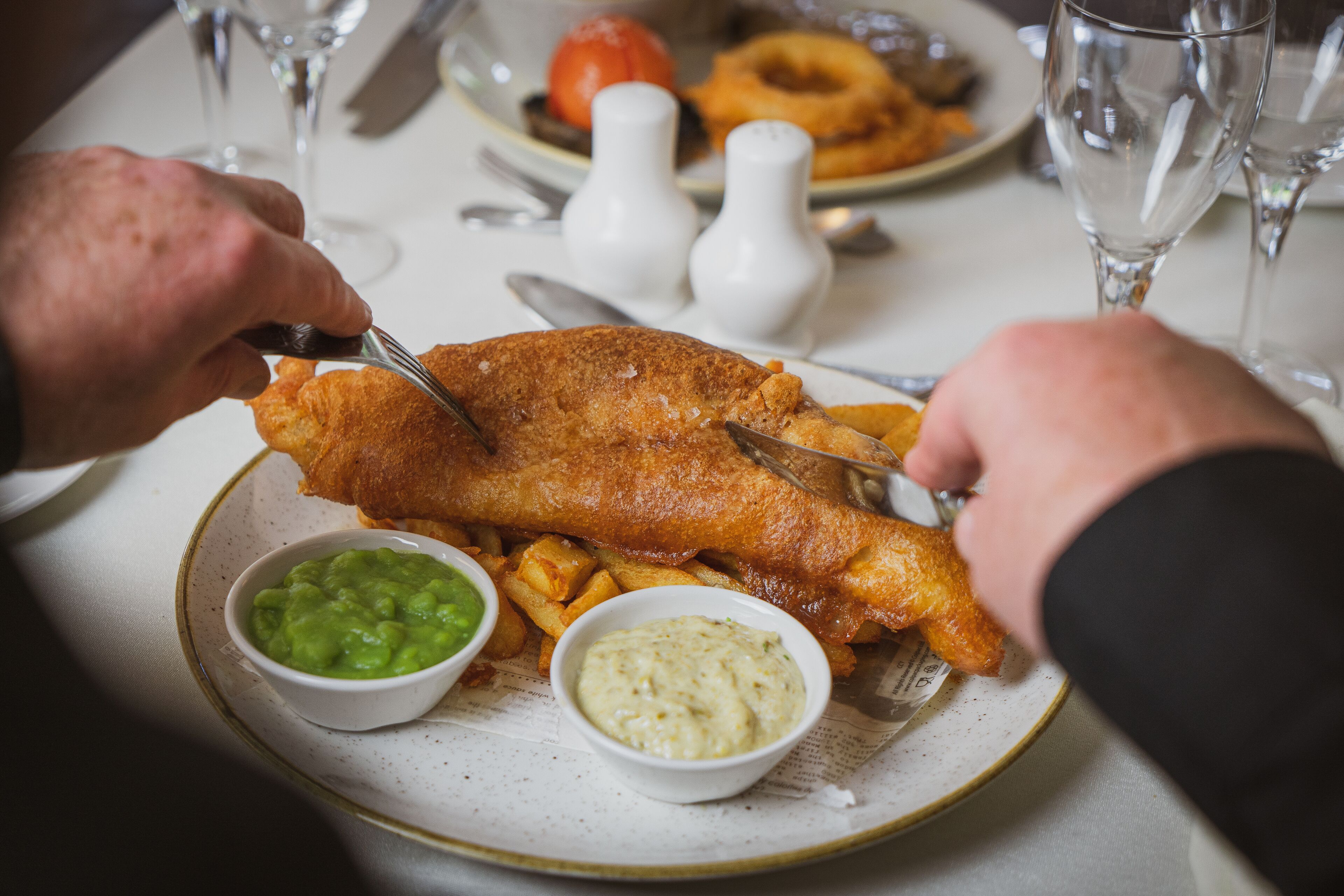 A plate of fish and chips with two dipping sauces and a glass of water.