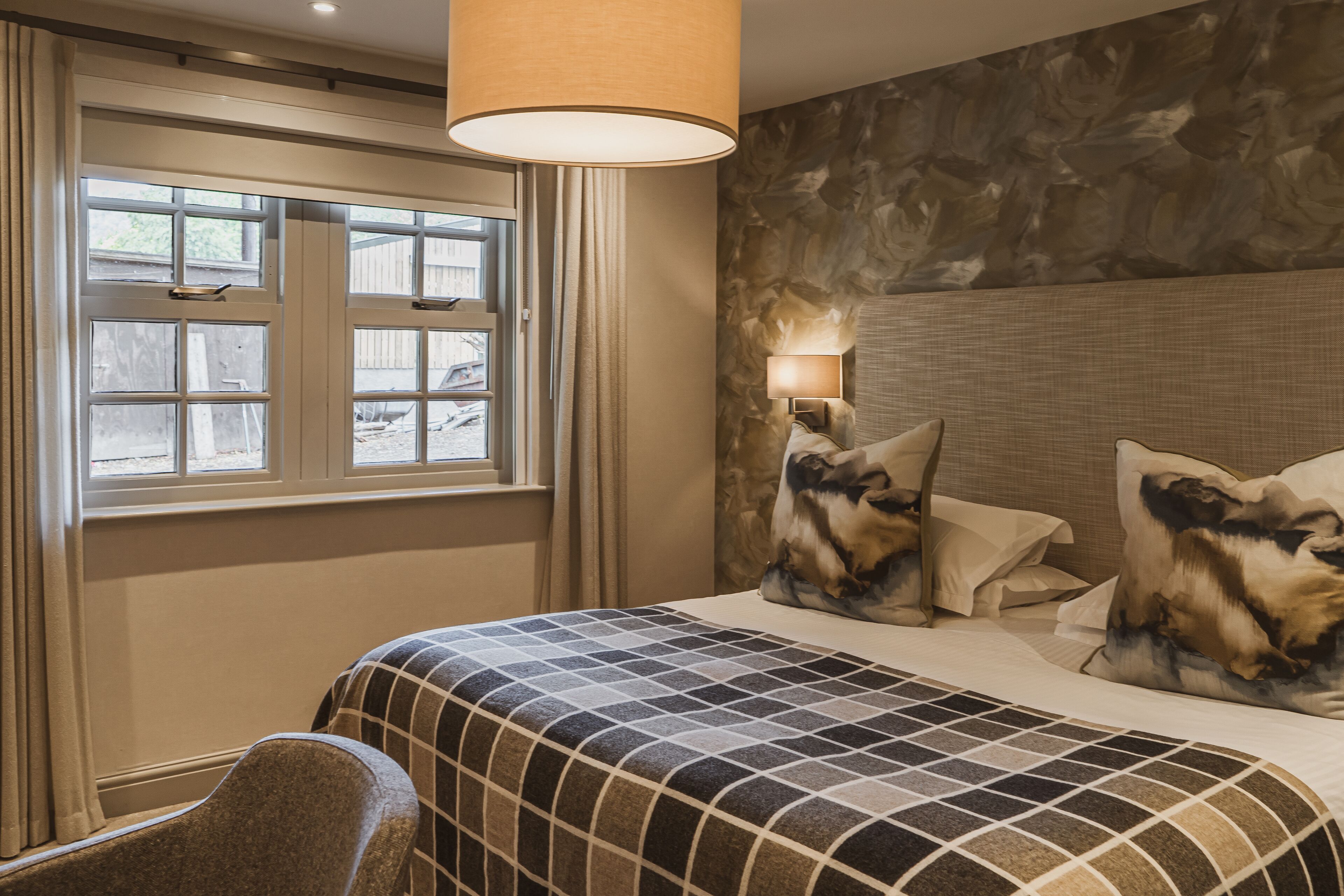 A hotel room with a large bed, a nightstand with a lamp, a window with curtains, and a wall with a textured pattern.