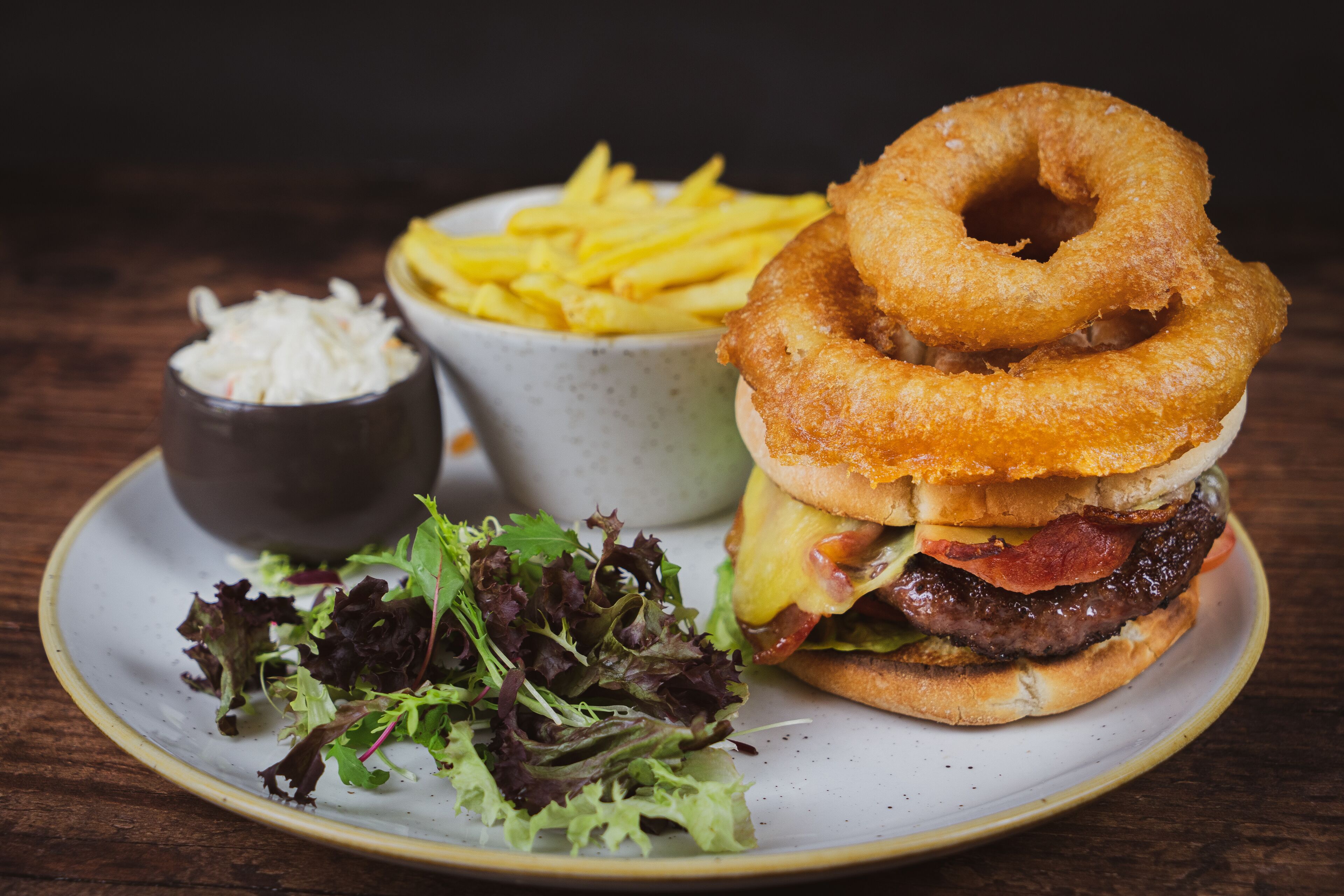 A plate with a burger, onion rings, fries, and a small bowl of salad.