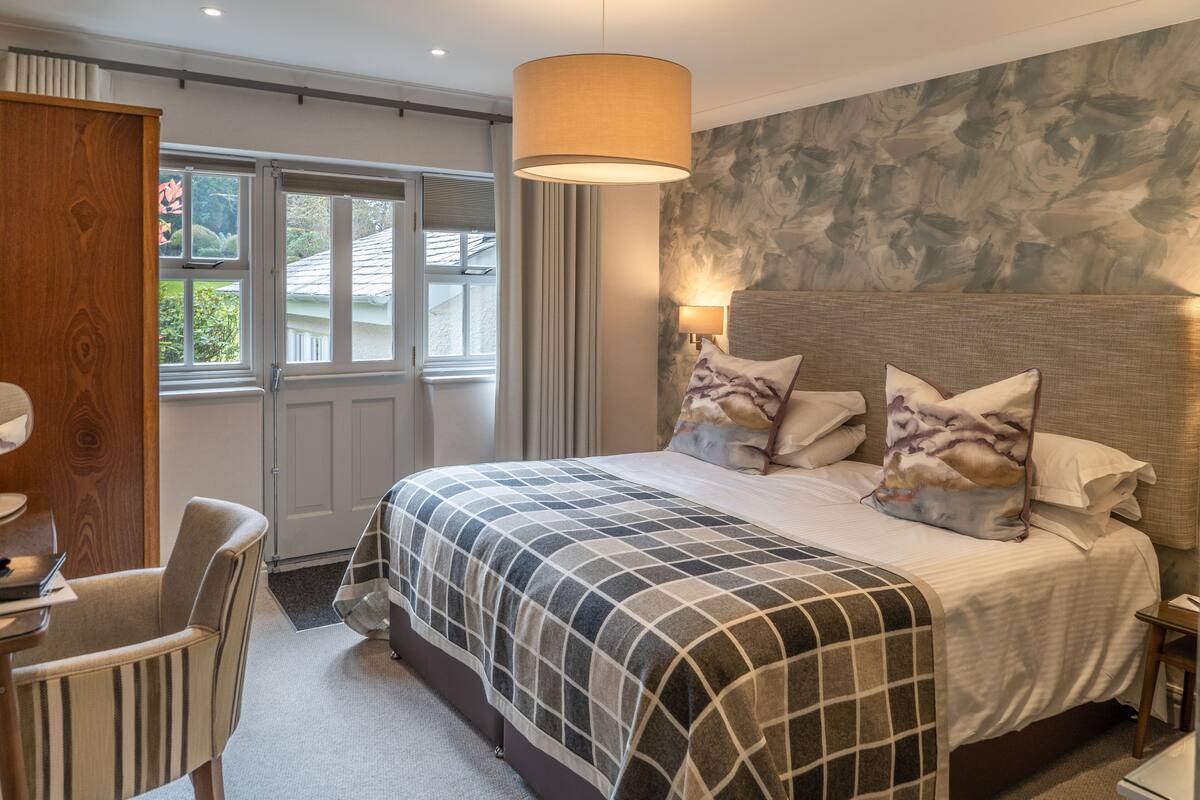 Hotelkamer met een groot bed, een bureau met stoel, een raam met gordijnen en een wand met een structuur.