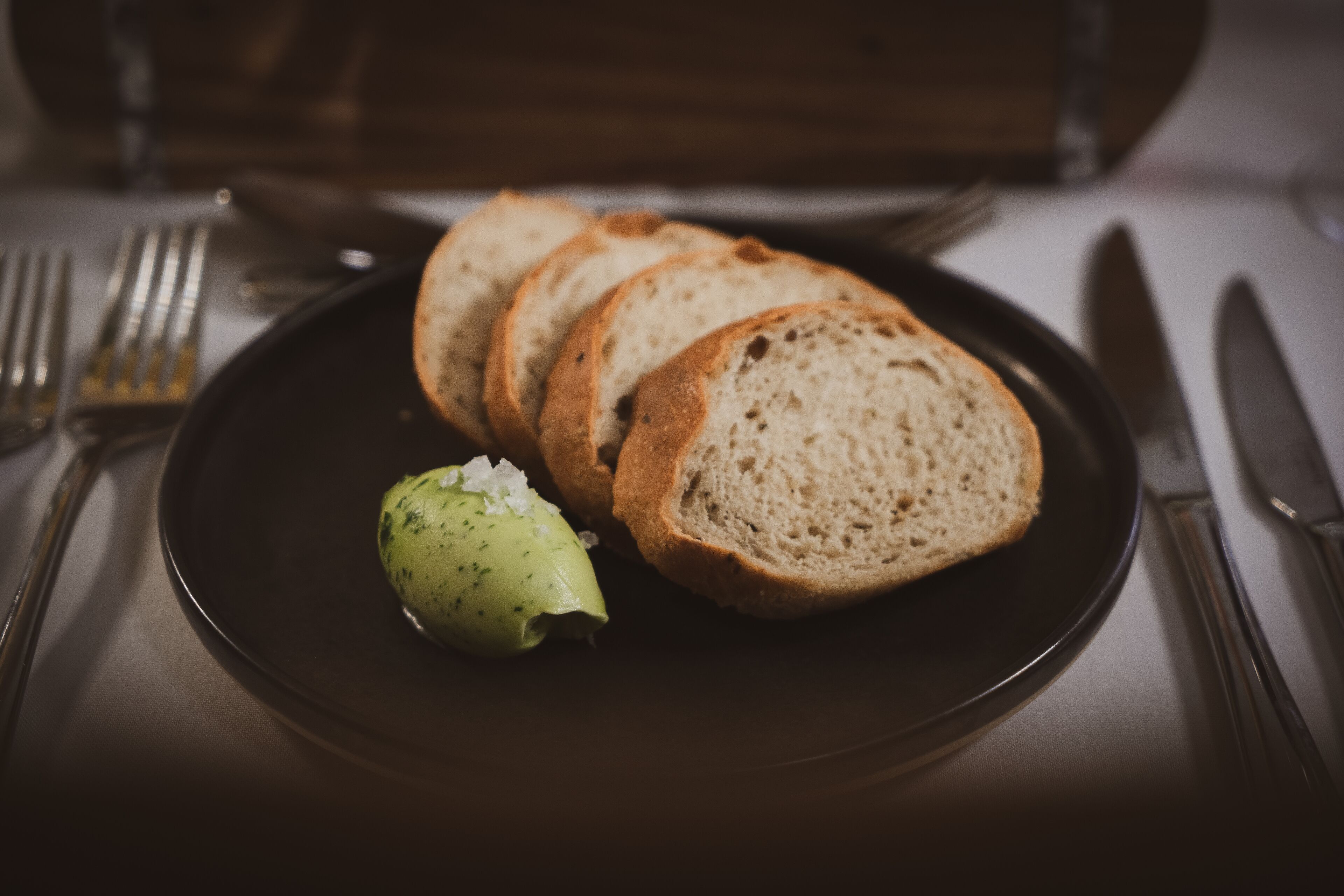 A plate with slices of bread and a dollop of butter on a dark plate.