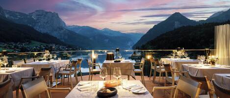 Un restaurante con mesas dispuestas para comer, con vistas a un paisaje montañoso y una masa de agua.