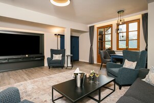 A modern living room with a flat-screen TV, comfortable seating, a coffee table, and a dining area with a table and chairs.