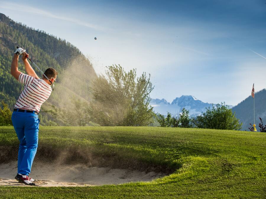 Un golfista en un campo verde, con cielo despejado y montañas al fondo.