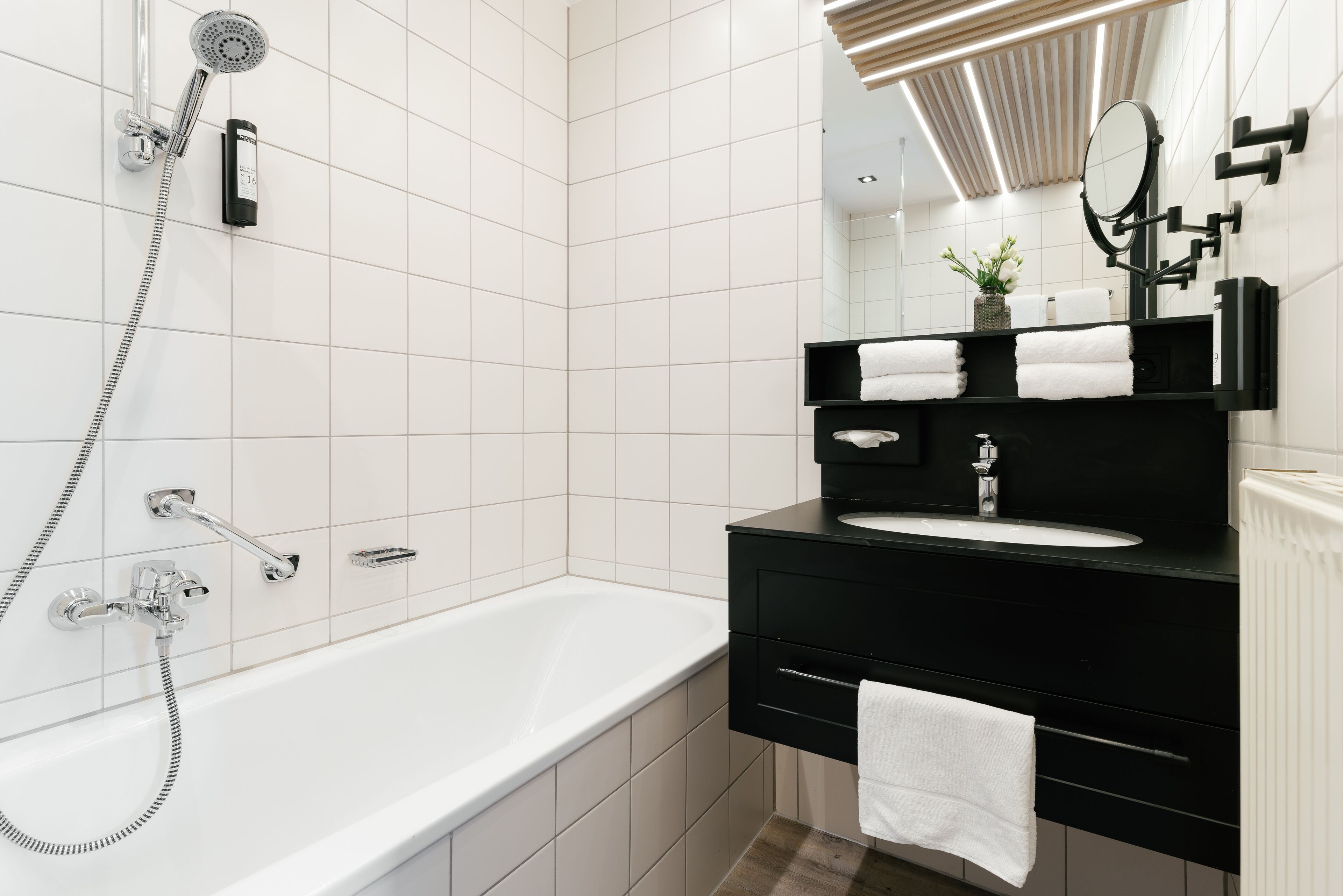 Un baño moderno con una bañera blanca, tocador negro y un espejo grande.