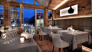 Un restaurante con interiores de madera, varias mesas dispuestas para comer y amplias ventanas con vistas a las montañas.