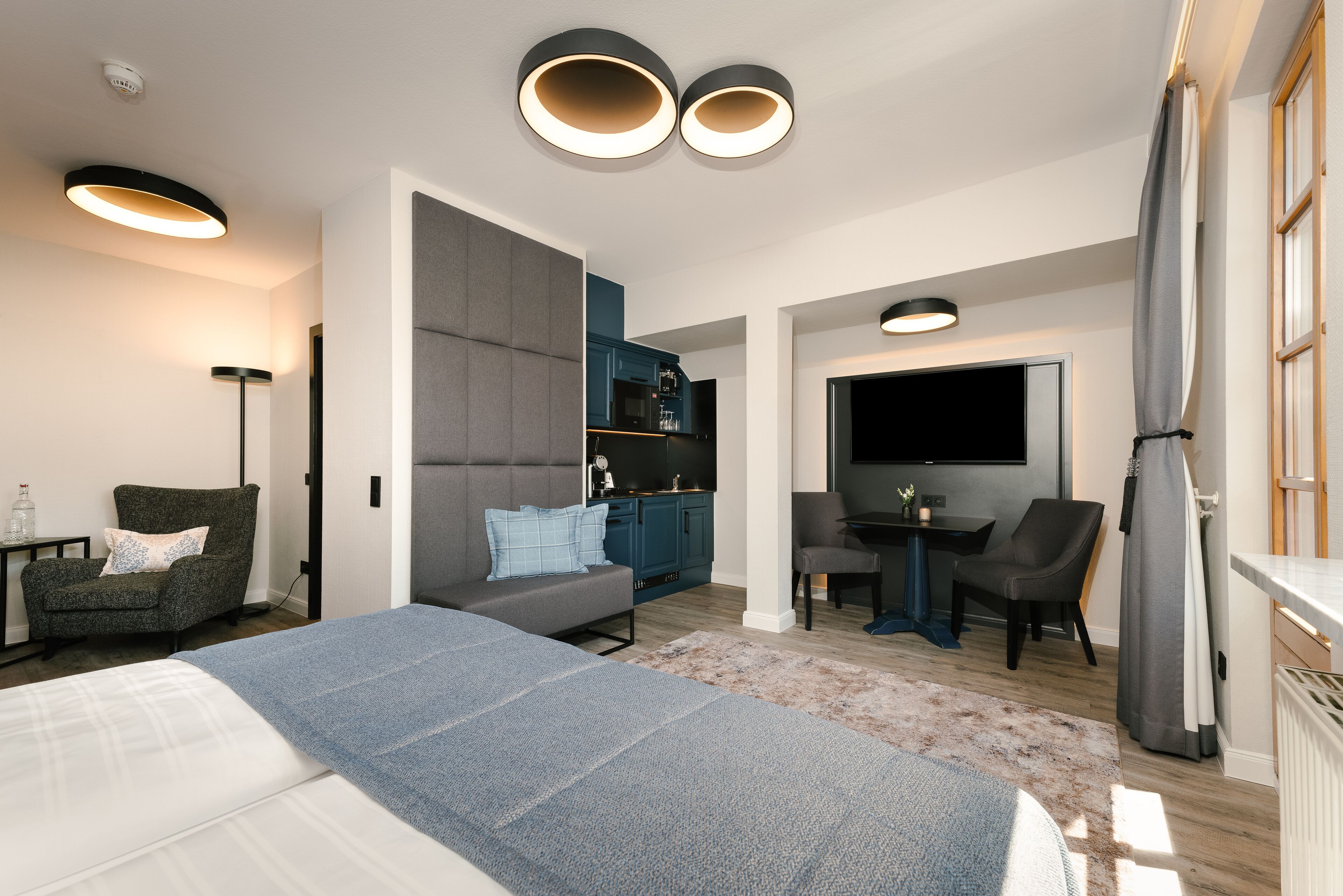 A modern hotel room with a large bed, a sofa, a desk, a TV, and a wardrobe.
