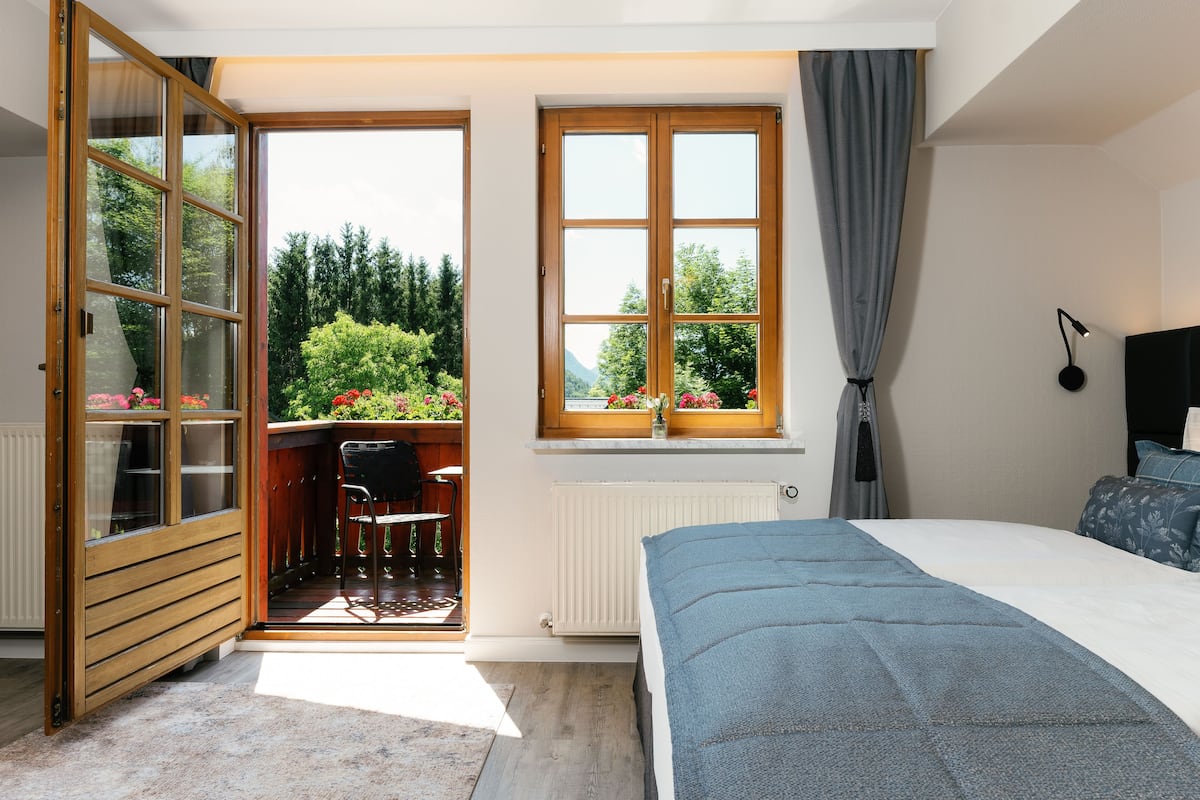 A bedroom with a bed, a window with curtains, a radiator, and a view of greenery outside.
