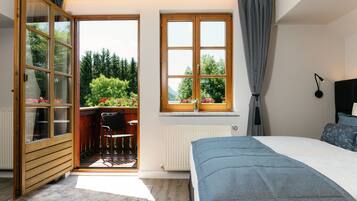 Un dormitorio con cama, ventana con cortinas, radiador y vistas a zonas verdes.