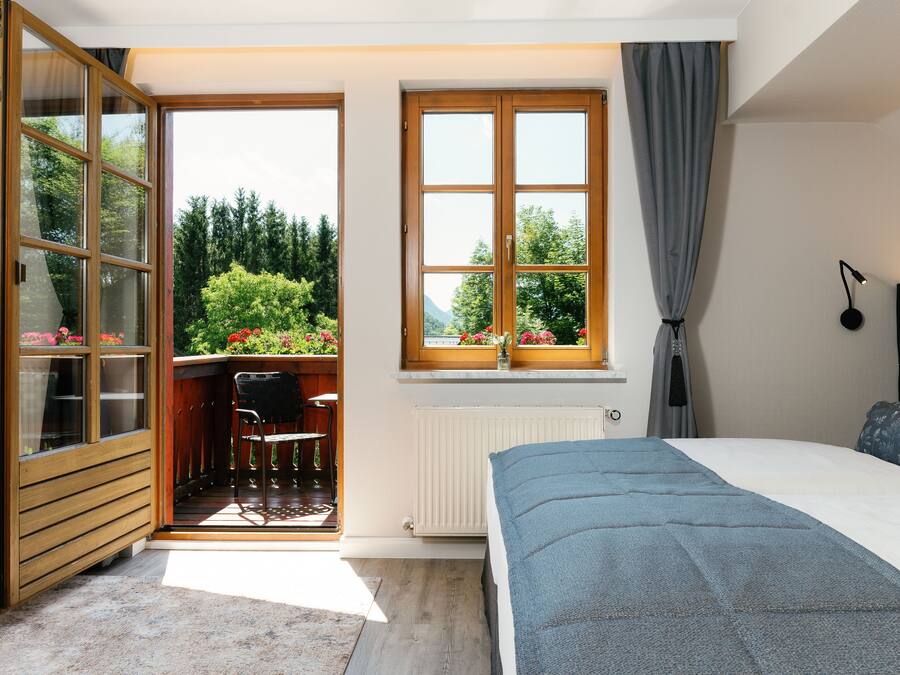 Un dormitorio con cama, ventana con cortinas, radiador y vistas a zonas verdes.