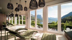 A modern room with large windows, green lounge chairs, and hanging black pendant lights. - MONDI Hotel am Grundlsee (Grundlsee)