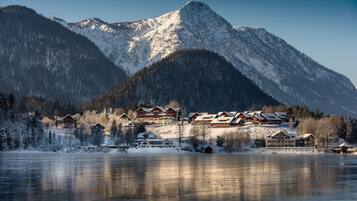 A mountain lodge with multiple buildings, a frozen lake in the foreground, and snow-covered mountains in the background.