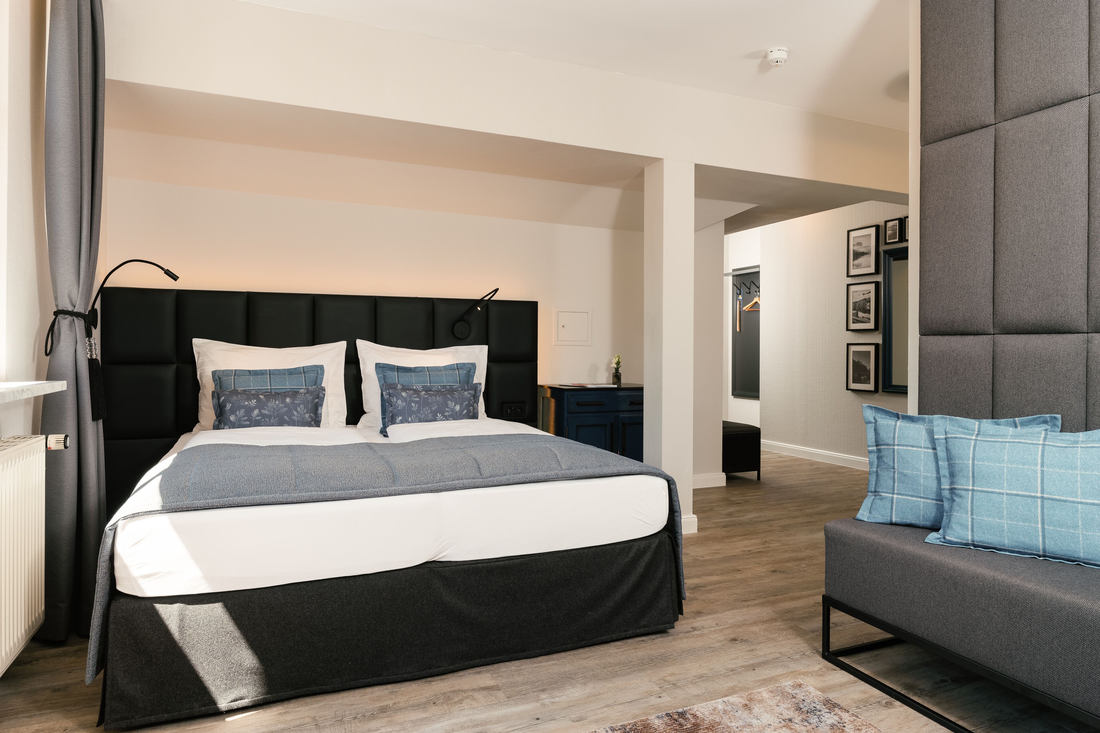 Ein modernes Schlafzimmer mit einem großen Bett, einem grauen Polstersofa und Holzboden.