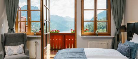 Un dormitorio con una cama grande, una silla y dos ventanas con vistas a la montaña.