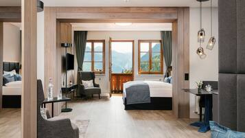 Una habitación de hotel moderna con dos camas, una zona de estar con una silla y una mesa, televisión y ventanas amplias con vistas a la montaña.
