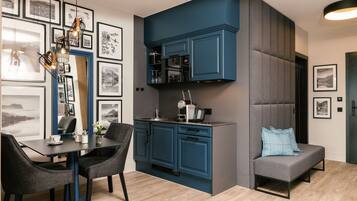 Eine moderne Küche mit blauen Schränken, ein Essbereich mit Tisch und Stühlen sowie ein graues Sofa mit einem blauen Kissen.