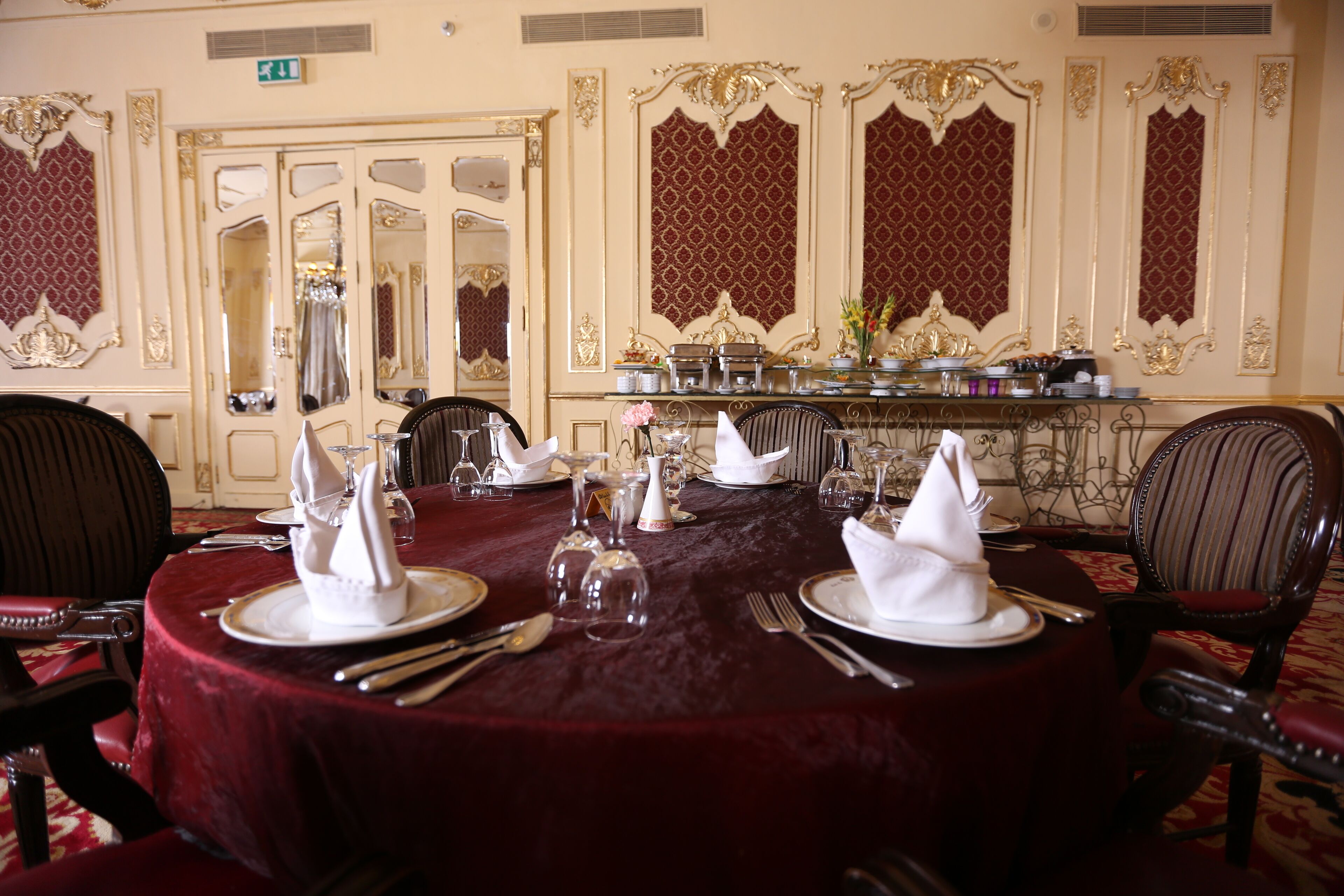 A formal dining room with round tables set for a meal, chairs, and a buffet area.