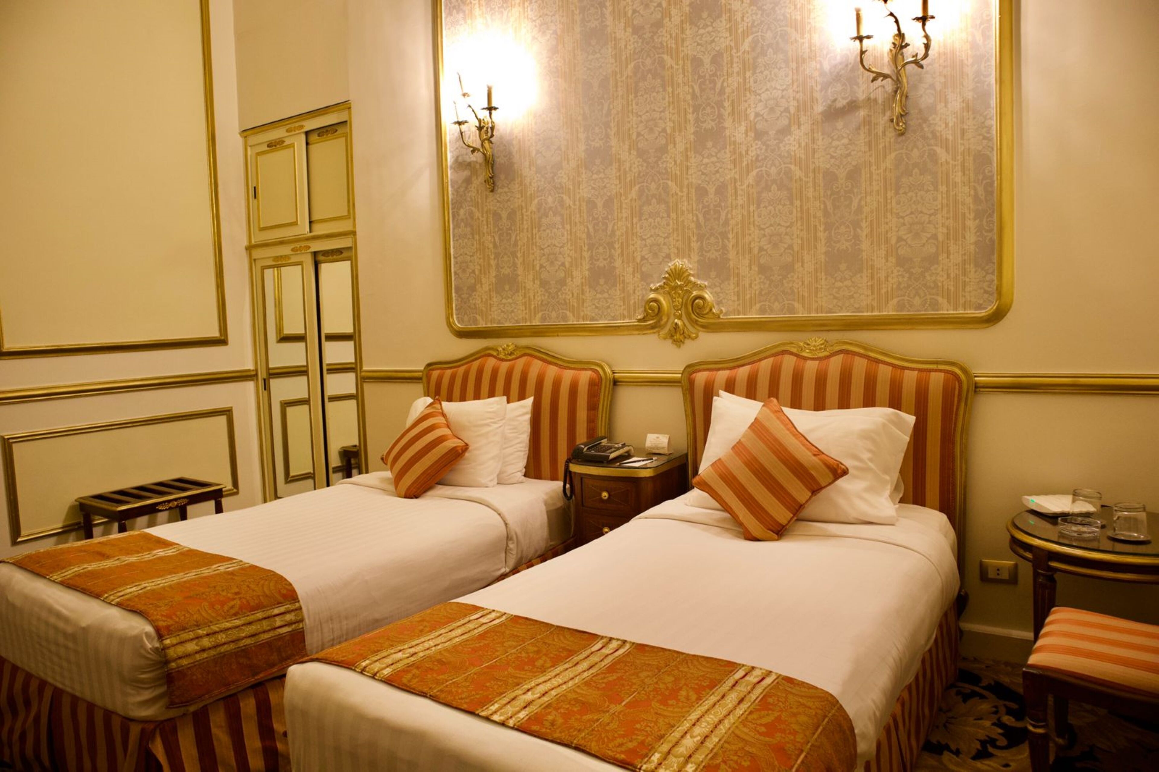 Habitación de hotel con dos camas, un espejo, una mesita de noche y una pequeña mesa con vasos.