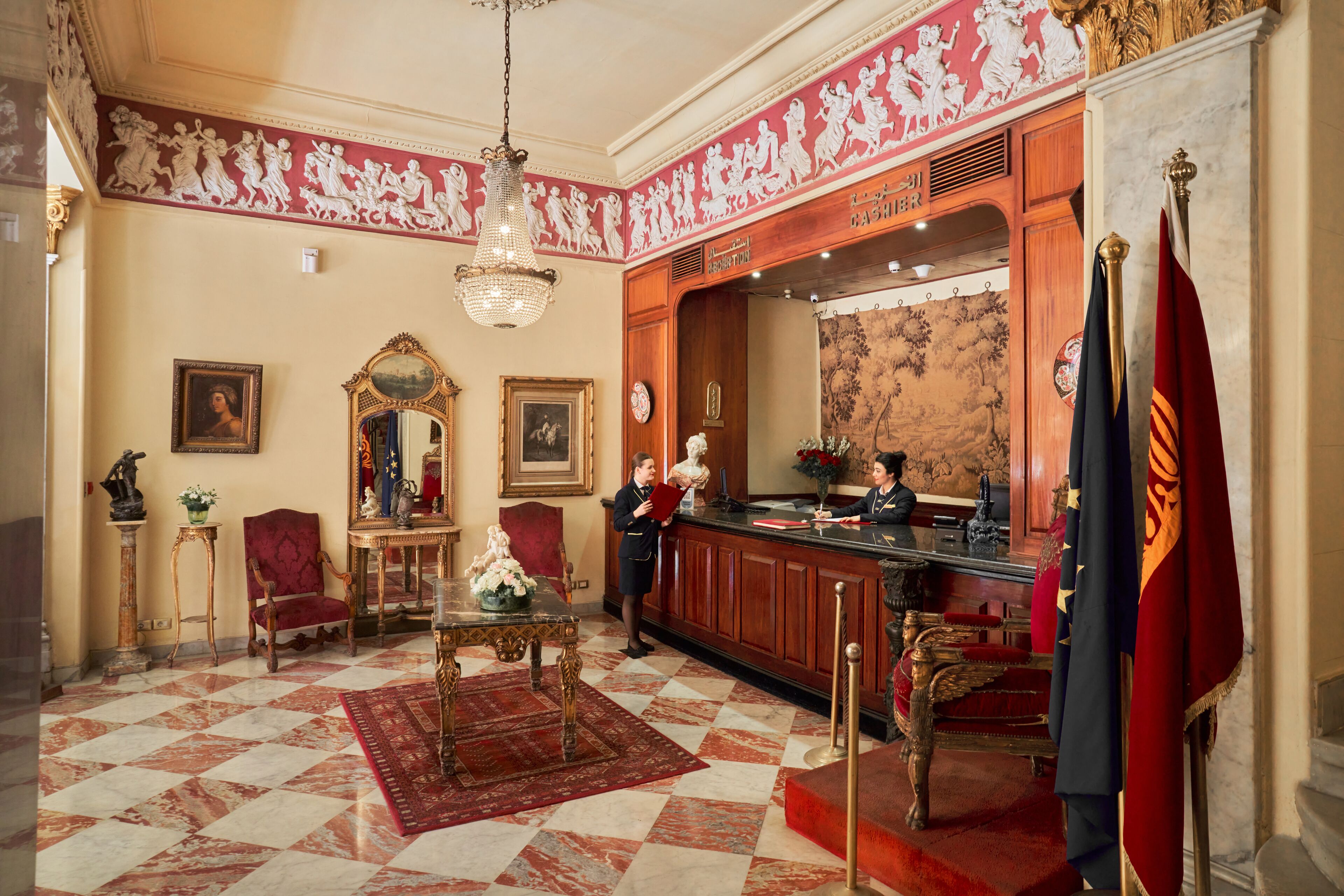 Un vestíbulo con piso a cuadros, una recepción, un espejo y un candelabro.
