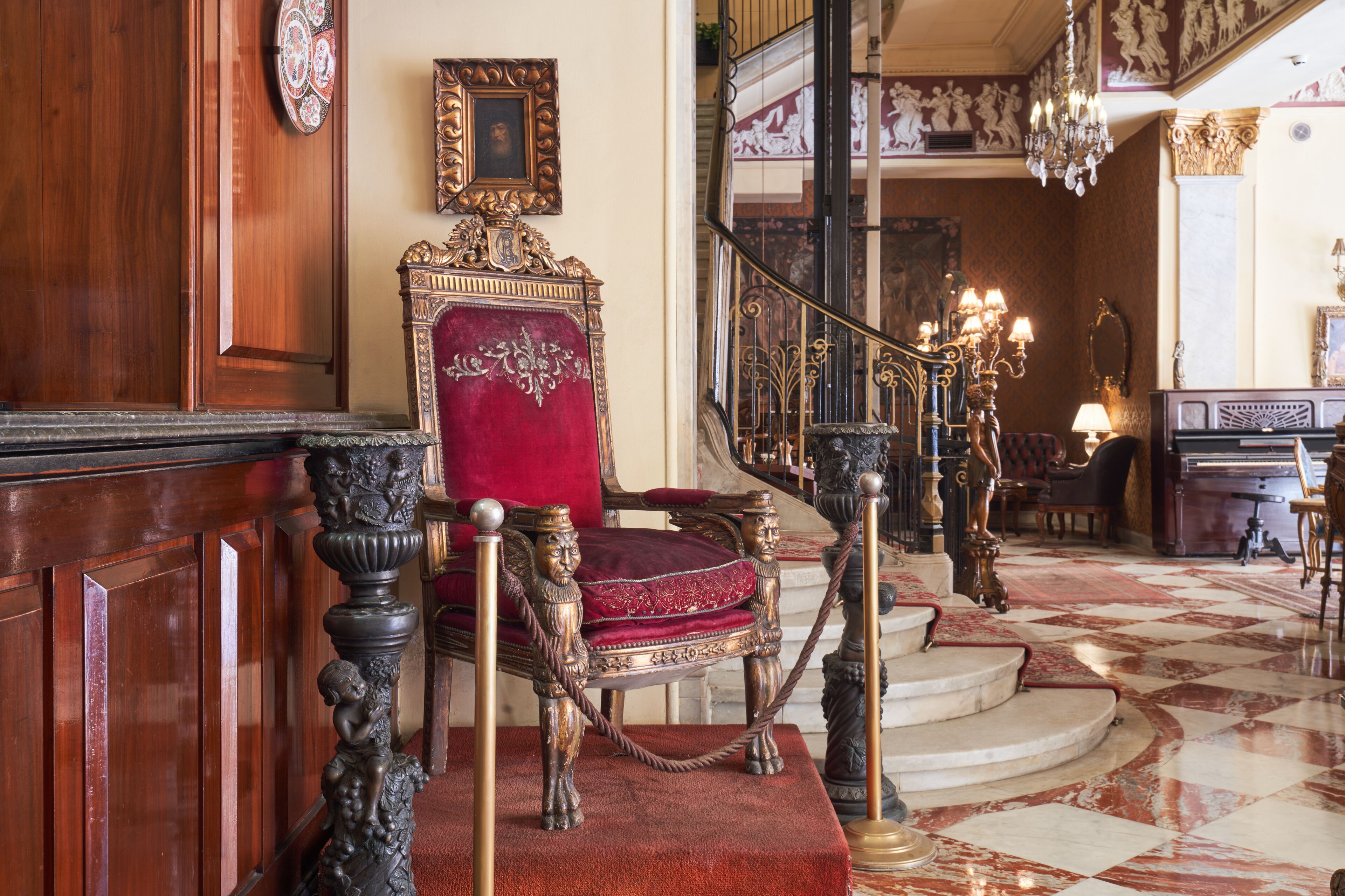 A grand staircase with ornate railings and a red velvet chair at the top.