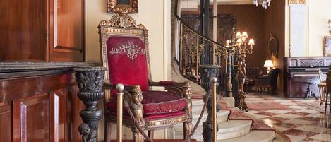 A grand staircase with ornate railings and a red velvet chair at the top.