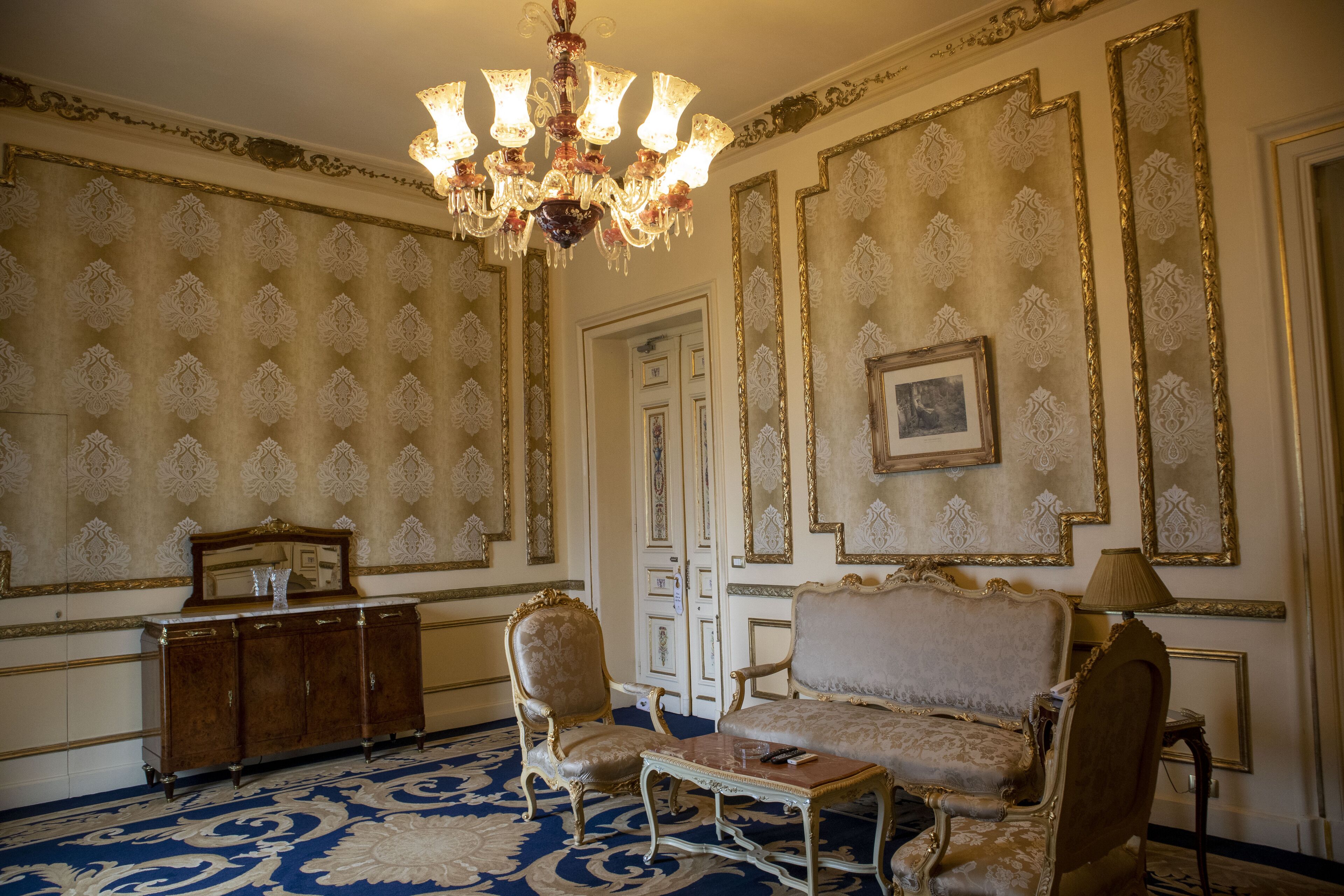 Una habitación con candelabro, papel tapiz decorativo, un sofá, una silla y una mesita.