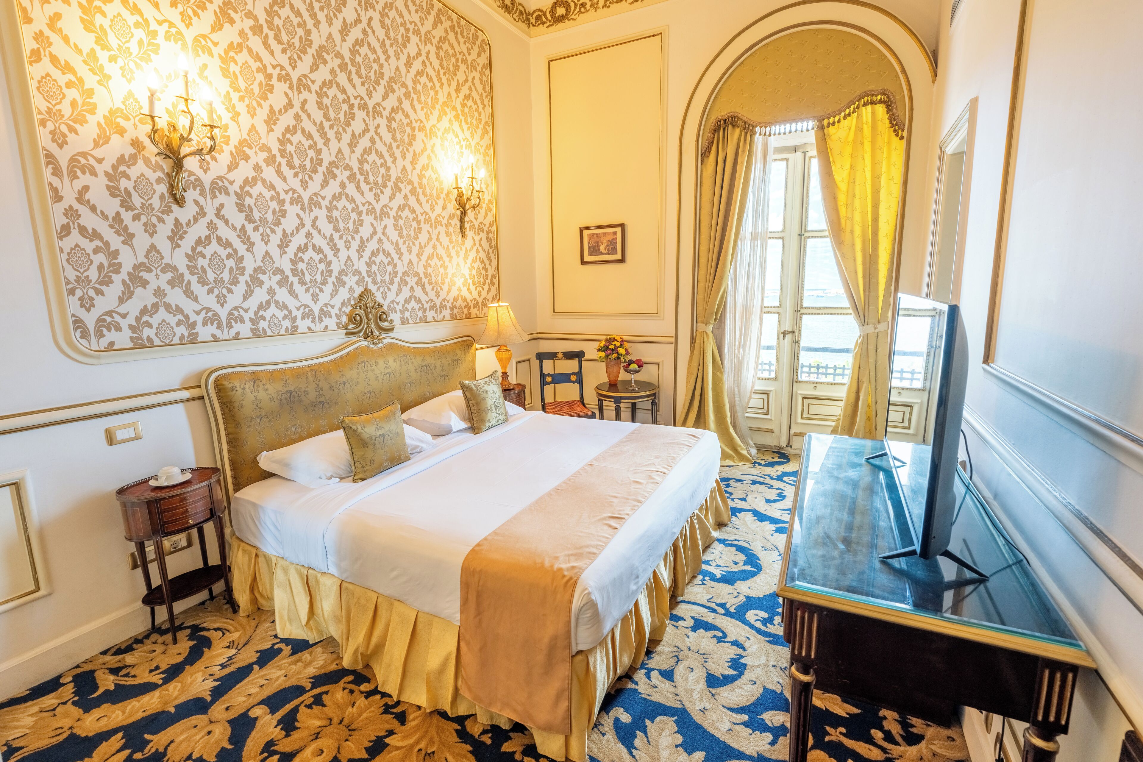 A hotel room with a large bed, a desk, a chair, a small table, and a window with curtains.