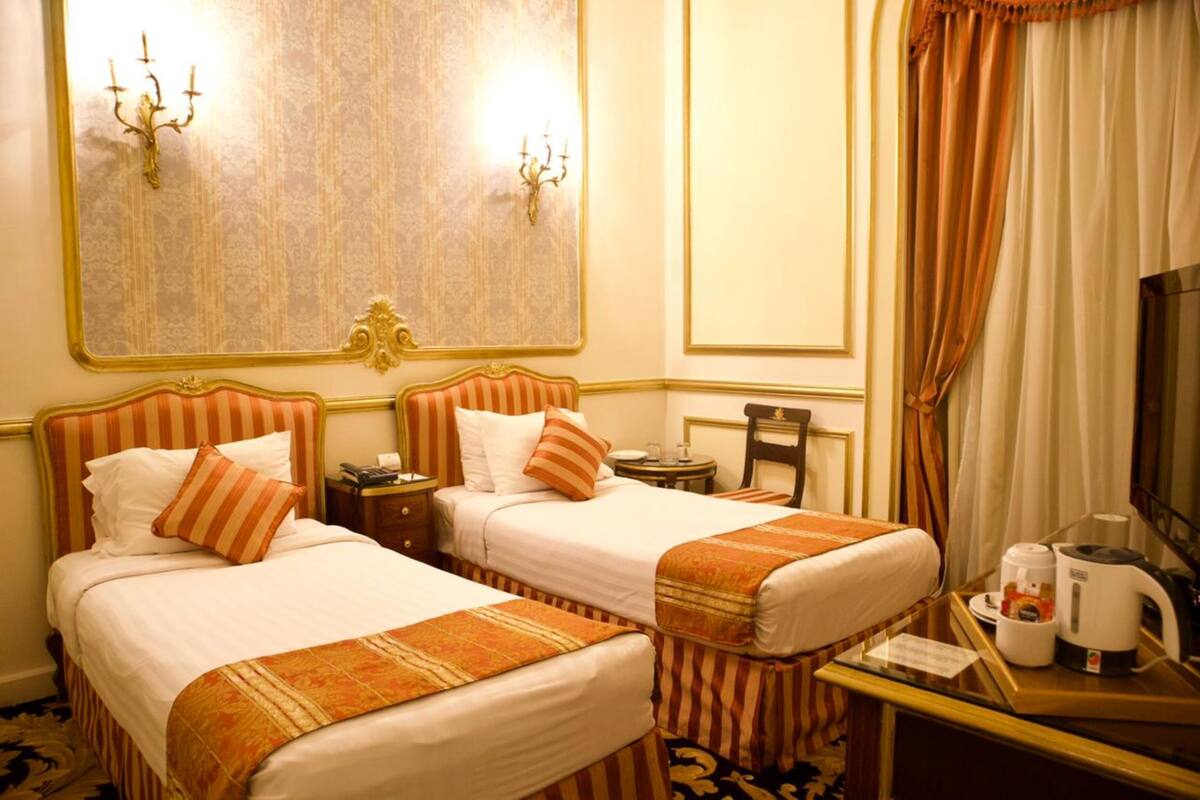 A hotel room with two beds, a desk with a coffee maker, a mirror, and a large wall decoration.