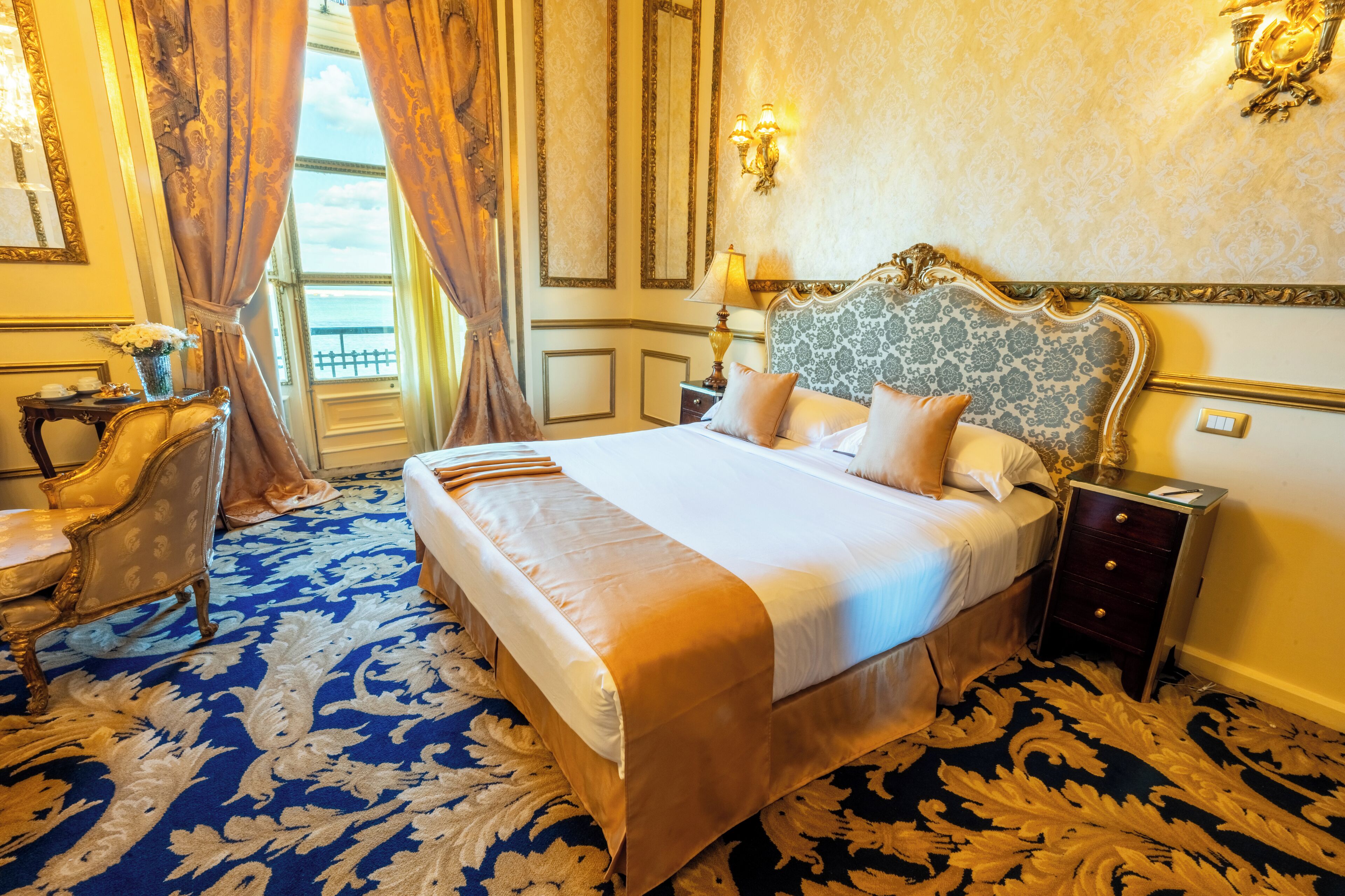 Ein luxuriöses Hotelzimmer mit einem großen Bett, einem verzierten Kopfteil und einem blauen Teppich mit Muster.