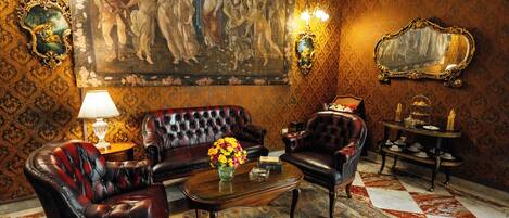A room with a large ornate painting, a tufted leather sofa, a coffee table with a vase of flowers, and a patterned rug.