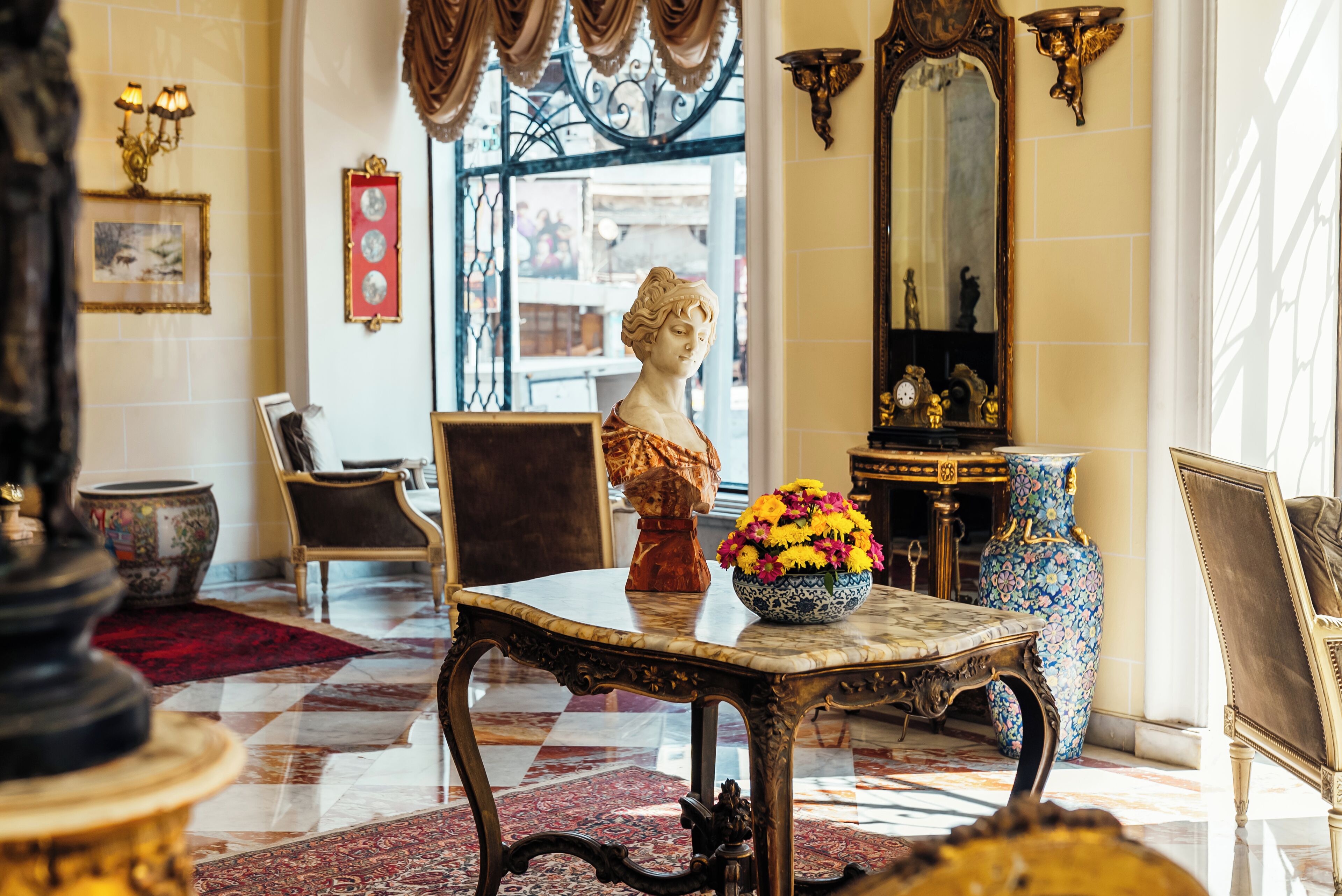 Een luxueuze lobby met een marmeren vloer, decoratief meubilair en een borstbeeld.