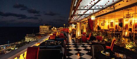 A rooftop restaurant with a checkered floor, outdoor seating, and a view of the city skyline.