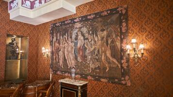 A room with ornate wallpaper, a large classical painting, a marble-topped table, and a statue.