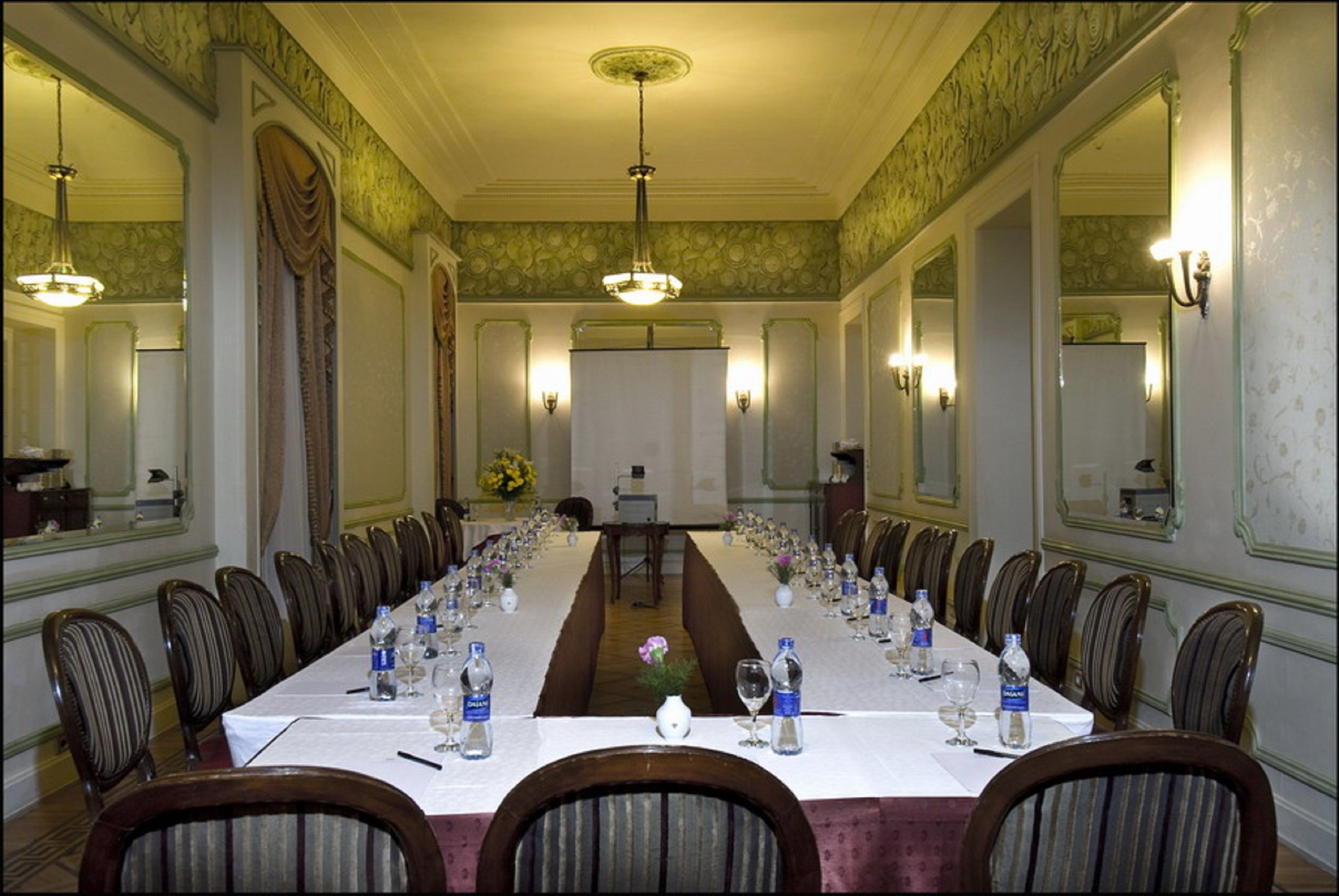 A long conference table set for a meeting with chairs around it, in a room with ornate wall decorations and chandeliers.