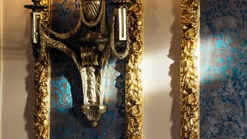 A wall-mounted light fixture with two candles, ornate gold detailing, and a blue patterned backdrop.