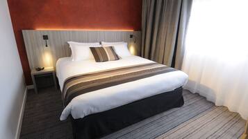 Une chambre d’hôtel avec un grand lit, une table de chevet, une lampe fixée au mur et une fenêtre avec des rideaux.