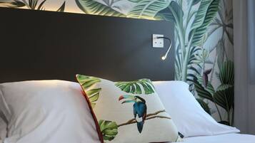 Una cama con sábanas blancas y una almohada con diseño de ave tropical.