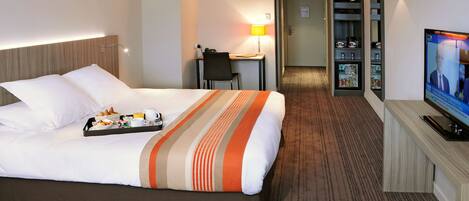 A hotel room with a bed, breakfast tray, desk, chair, TV, and a minibar.